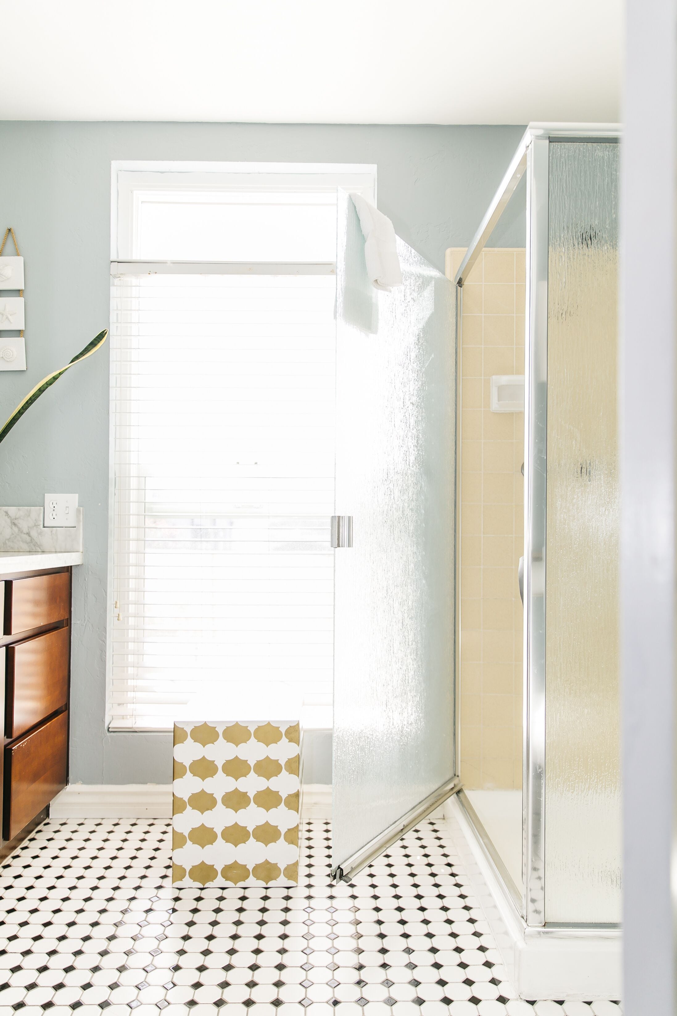 A bathroom with a white door, a shower enclosure, a patterned rug, and a tiled floor.
