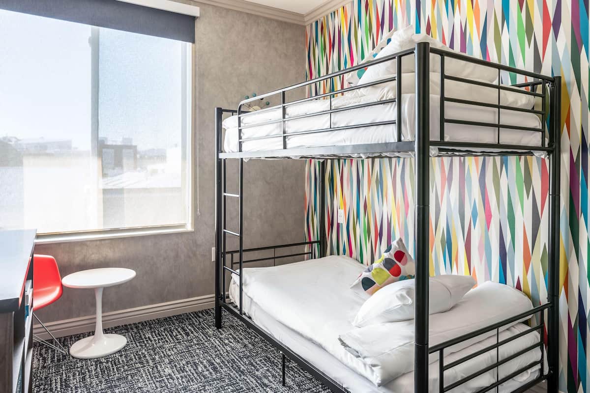 A bunk bed with white bedding, a small round table, and a colorful geometric-patterned wall.