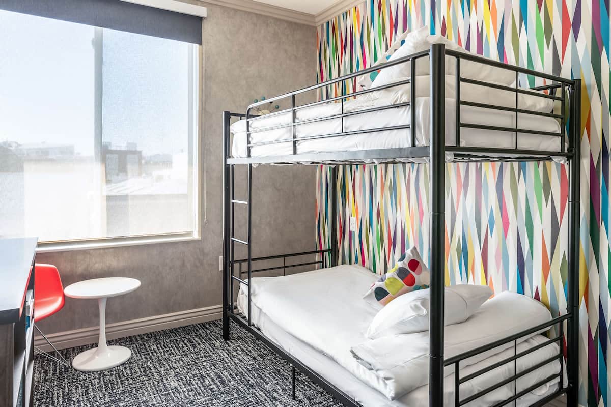 A bunk bed with white bedding, a small round table, and a colorful geometric-patterned wall.