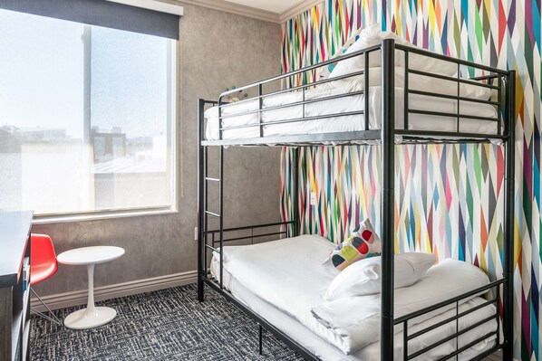A bunk bed with white bedding, a small round table, and a colorful geometric-patterned wall.