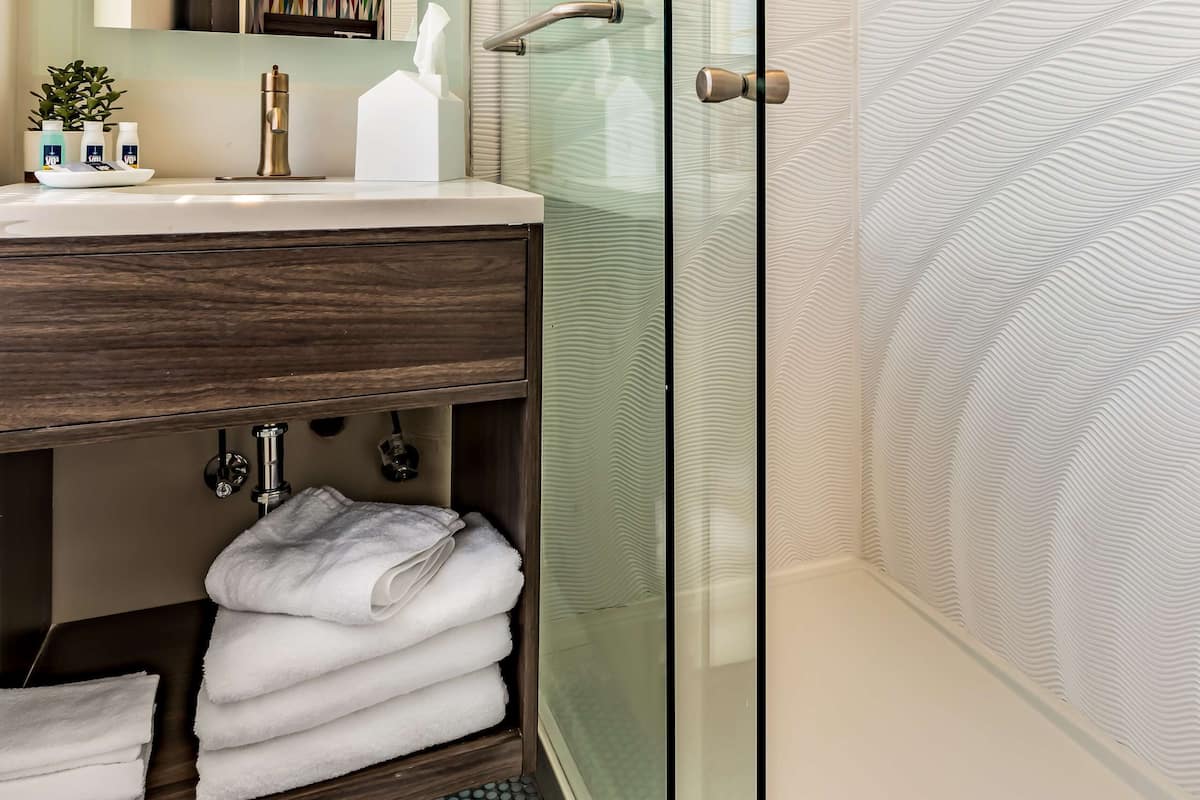 A modern bathroom with a glass shower enclosure, a wooden vanity with a mirror, and a tiled floor.