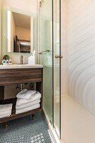 Un baño moderno con cabina de ducha de vidrio, tocador de madera con espejo y suelo de baldosas.