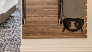 Ein ordentlich eingerichteter Raum mit einem Bett, einem an der Wand befestigten Bügelbrett und einem Kleiderständer mit Kleiderbügeln und einem Koffer.