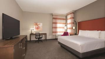 Habitación de hotel con una cama grande, un escritorio con silla, televisión y ventana con cortinas.