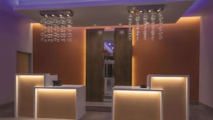 A reception area with two reception desks, a wooden wall, and a hanging light fixture. - La Quinta Inn & Suites by Wyndham South Jordan (South Jordan)