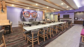 A modern dining area with multiple tables and chairs, a large mural on the wall, and a kitchen area in the background. - La Quinta Inn & Suites by Wyndham South Jordan (South Jordan)
