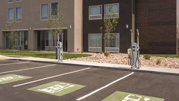 A parking area with electric vehicle charging stations, marked parking spaces, and a building with multiple windows and a modern design.