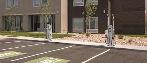 A parking area with electric vehicle charging stations, marked parking spaces, and a building with multiple windows and a modern design.
