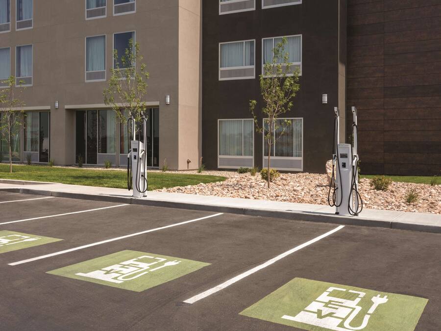 A parking area with electric vehicle charging stations, marked parking spaces, and a building with multiple windows and a modern design.