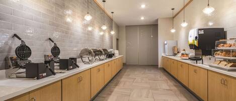 A modern kitchen with waffle makers, a coffee machine, and a bread display.
