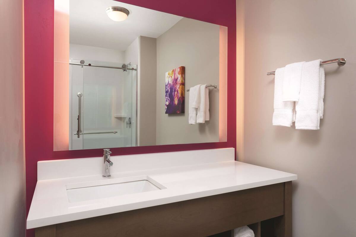 A modern bathroom with a white sink, a glass shower enclosure, and a mirror with a red frame.