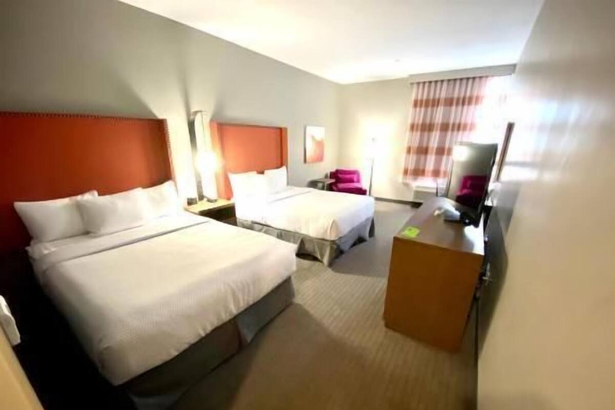 A hotel room with two beds, a desk, a chair, and a large window with curtains.