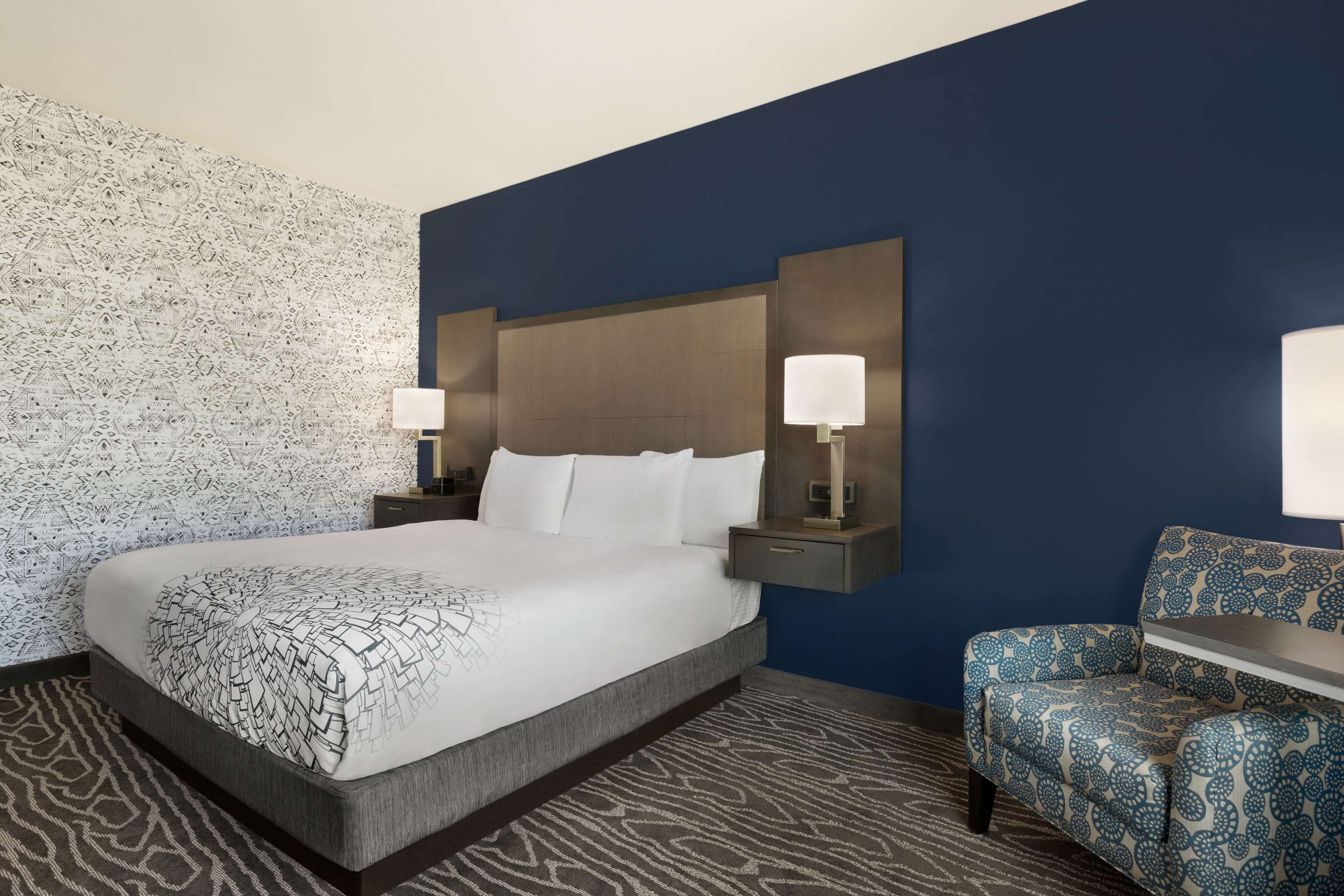 A hotel room with a large bed, two bedside tables with lamps, a patterned wall, a blue accent wall, and a patterned rug.