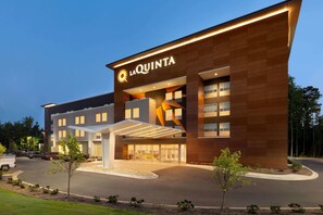 Un hotel moderno con un llamativo letrero de 'La Quinta', un acceso cubierto y un camino de entrada ajardinado.