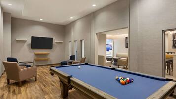 A pool table with balls, a flat-screen TV, and seating areas in a room with wooden flooring and neutral walls.