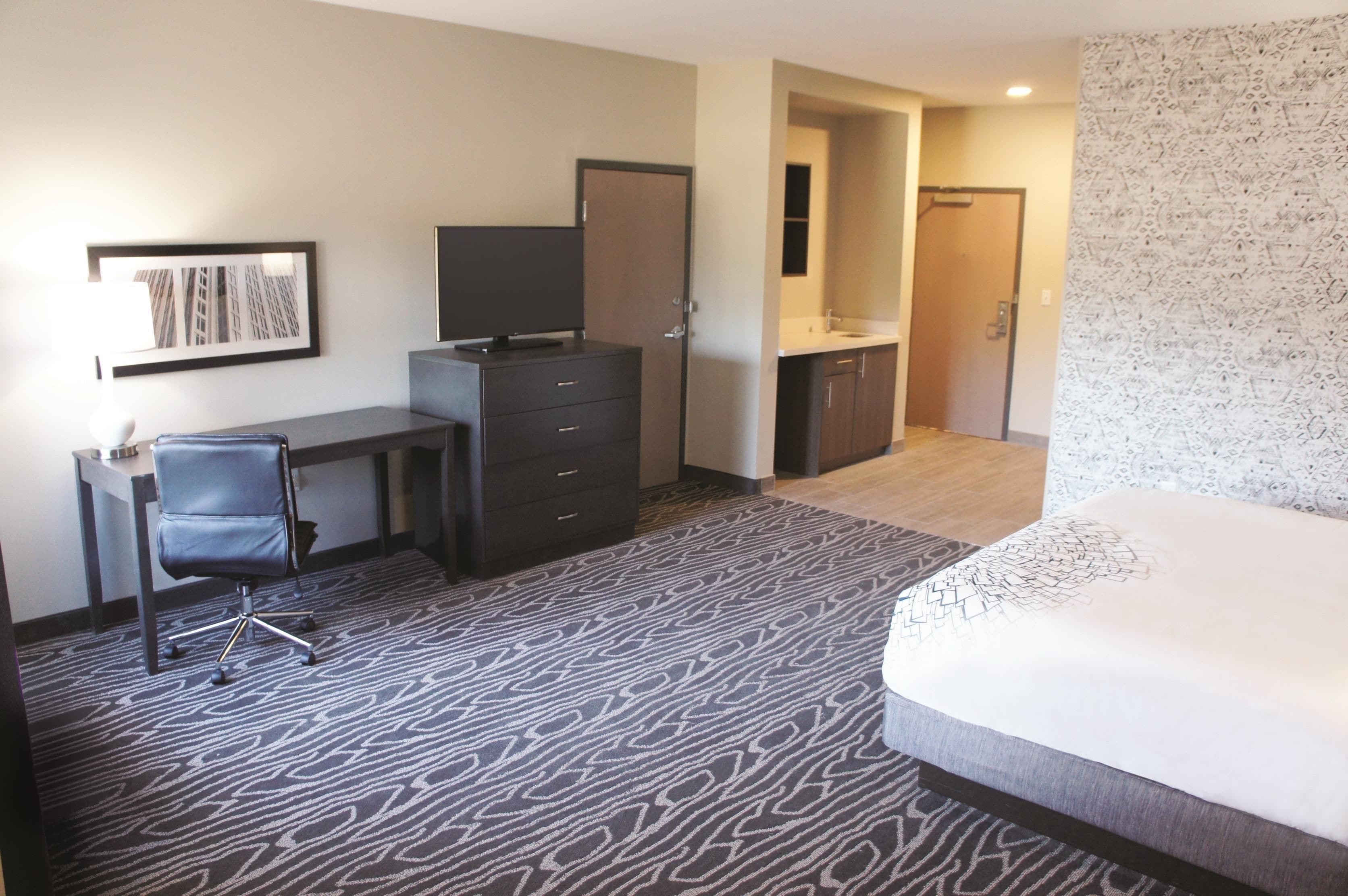 Une chambre d’hôtel comprenant un lit, un bureau avec une chaise, une commode, un miroir et une salle de bain avec un lavabo et des toilettes.