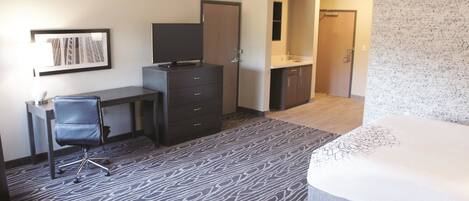 Une chambre d’hôtel comprenant un lit, un bureau avec une chaise, une commode, un miroir et une salle de bain avec un lavabo et des toilettes.