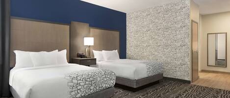 Une chambre d’hôtel avec deux lits, une table de chevet avec une lampe, un mur décoré et un miroir.