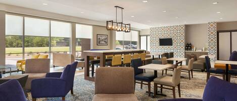 A hotel lobby with a bar area, seating arrangements, and large windows offering a view of the outdoors.