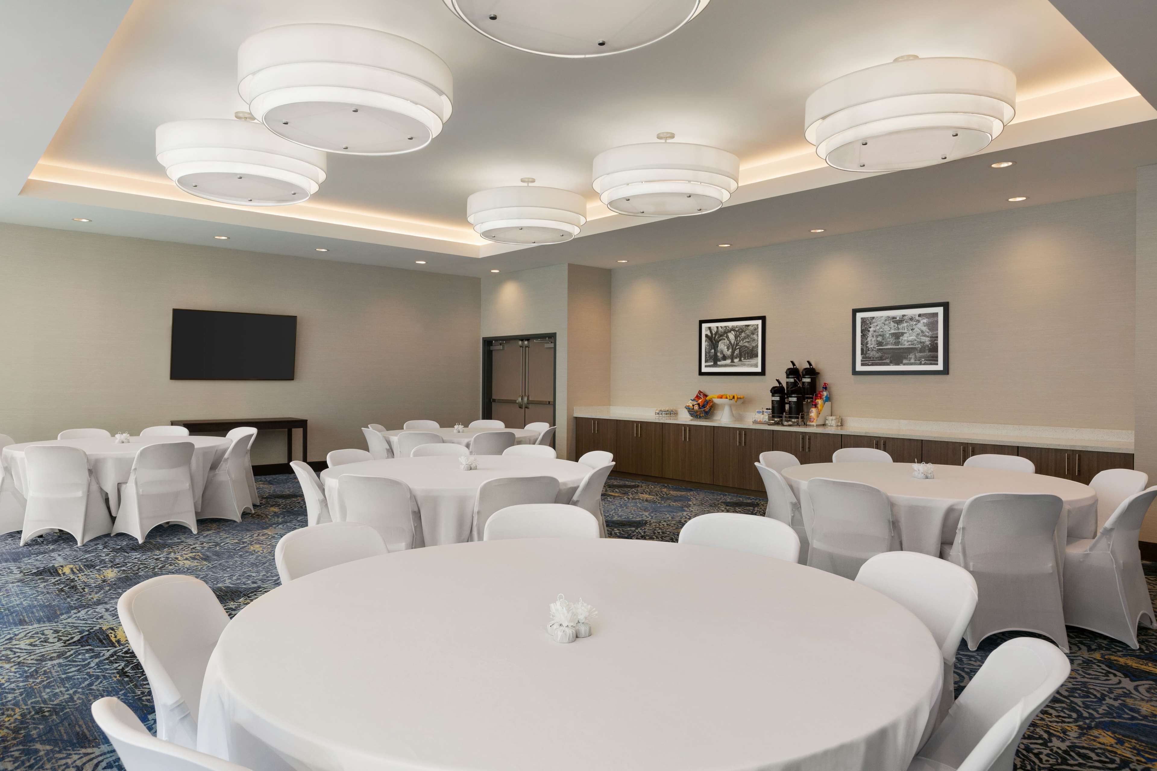 Une salle de conférence avec des tables rondes, des chaises blanches et des luminaires au plafond.
