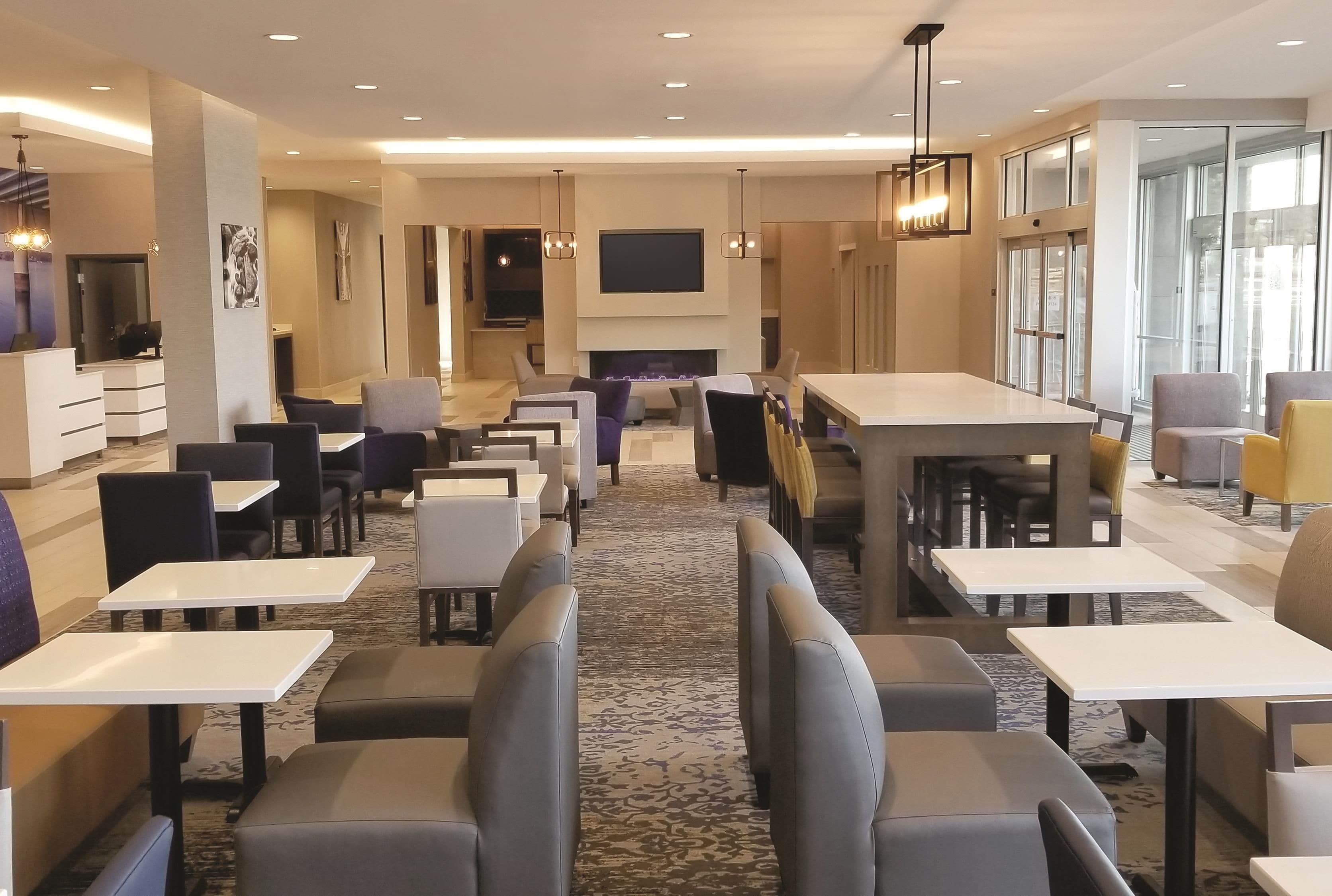 A modern hotel lobby with a central seating area, a fireplace, and a large TV screen.