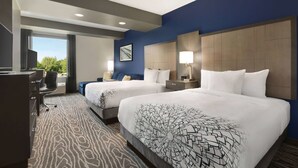 A hotel room with two beds, a desk, and a chair. There is a window with a view of greenery. - La Quinta Inn & Suites by Wyndham Rock Hill (Rock Hill)