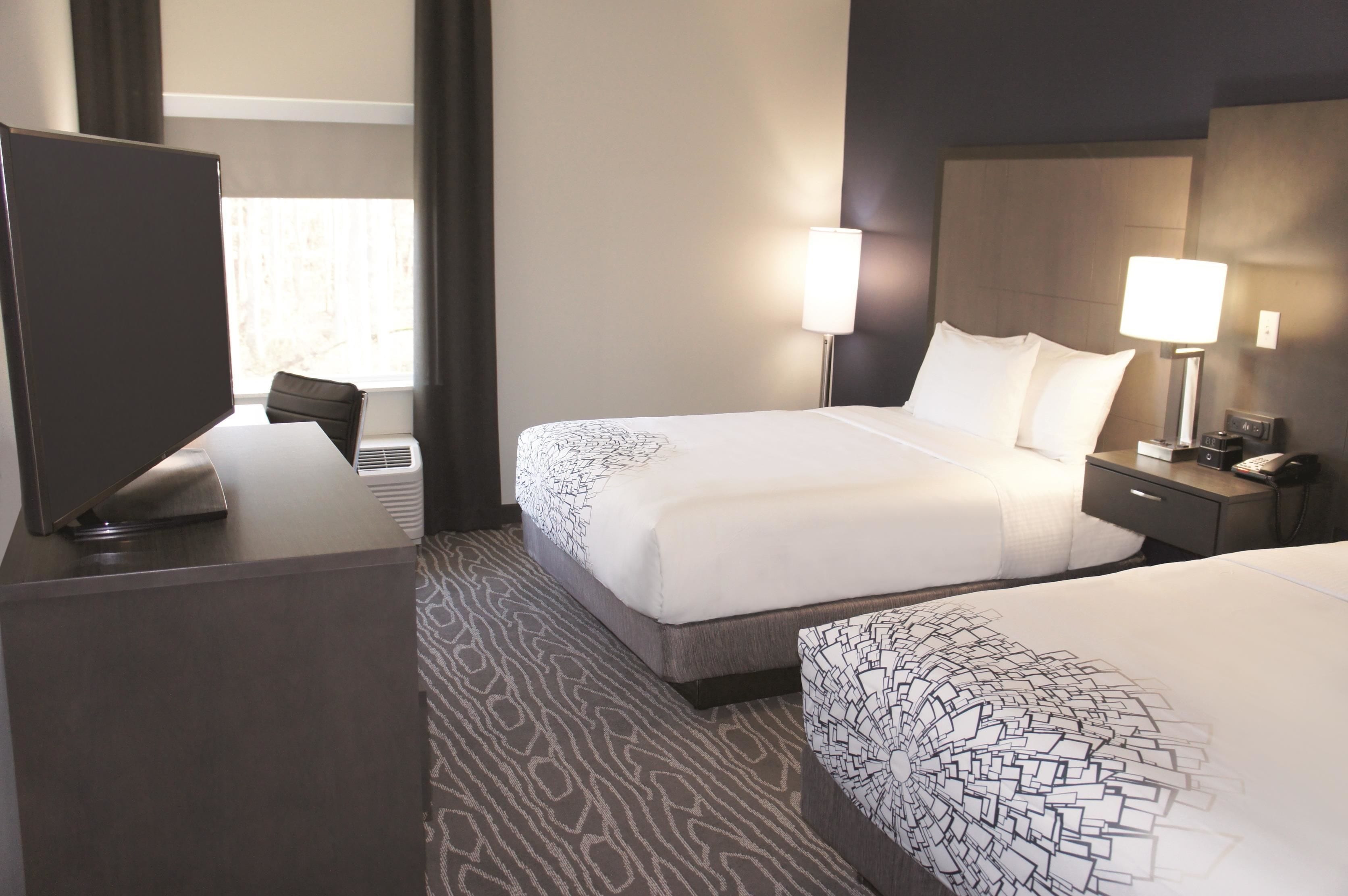 Habitación de hotel con dos camas, un escritorio y una silla. Hay dos lámparas de noche y una mesita con un teléfono.