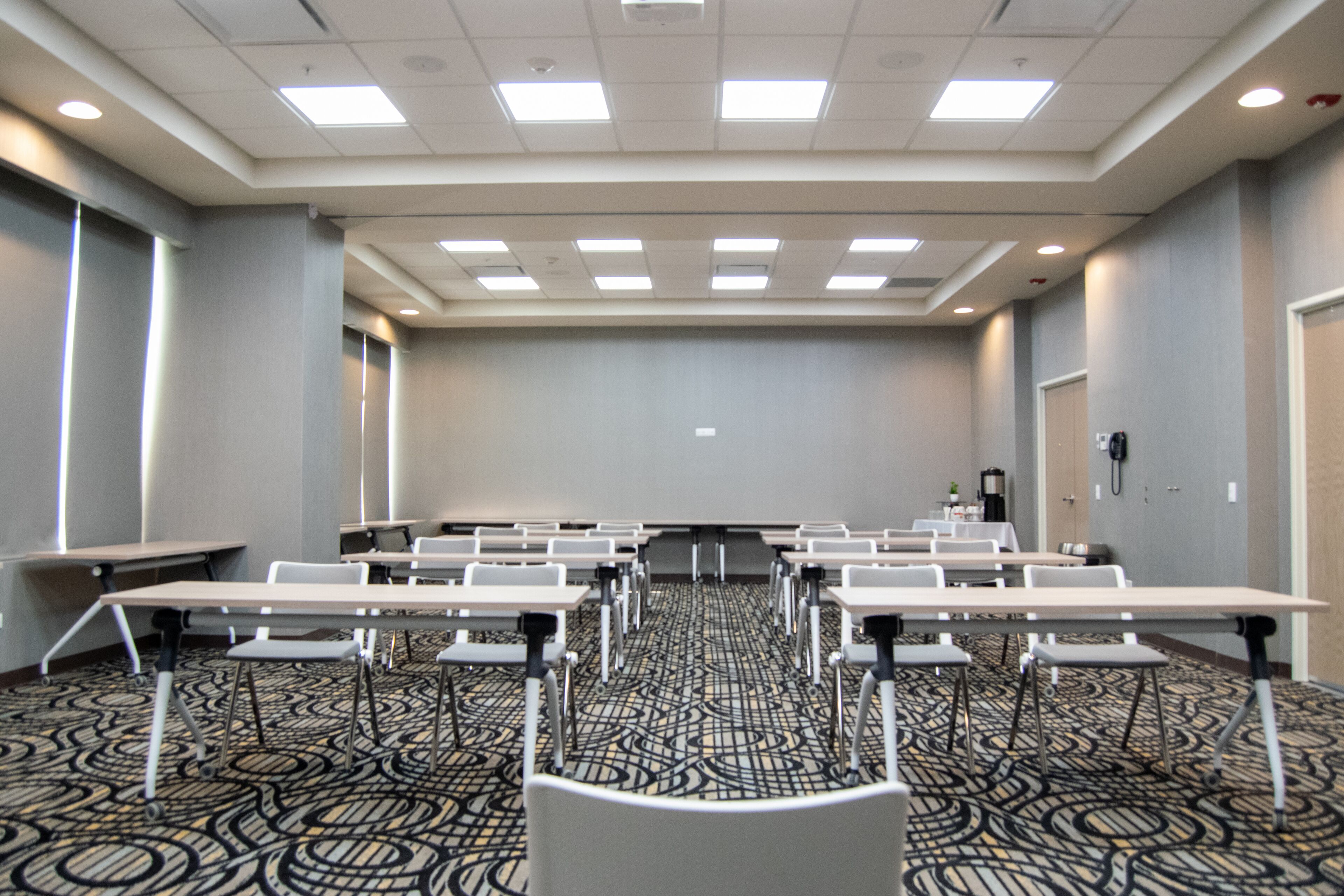 Un salón de conferencias con varias mesas y sillas, una pantalla de proyector y una alfombra estampada.