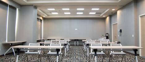 Un salón de conferencias con varias mesas y sillas, una pantalla de proyector y una alfombra estampada.