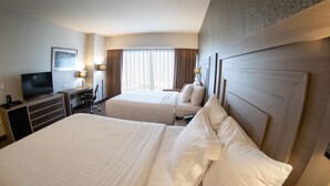 Una habitación de hotel con dos camas, un escritorio con televisor y una ventana con cortinas.
