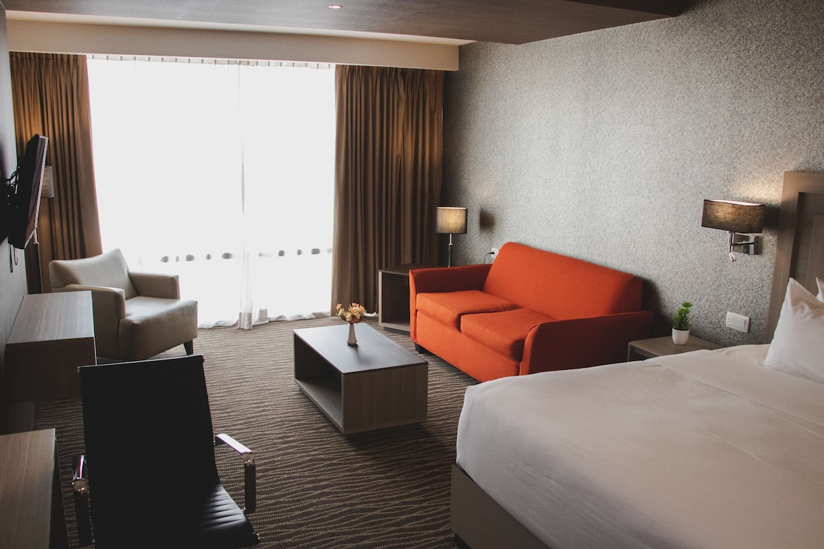 A hotel room with a bed, a sofa, a chair, a coffee table, and a TV.
