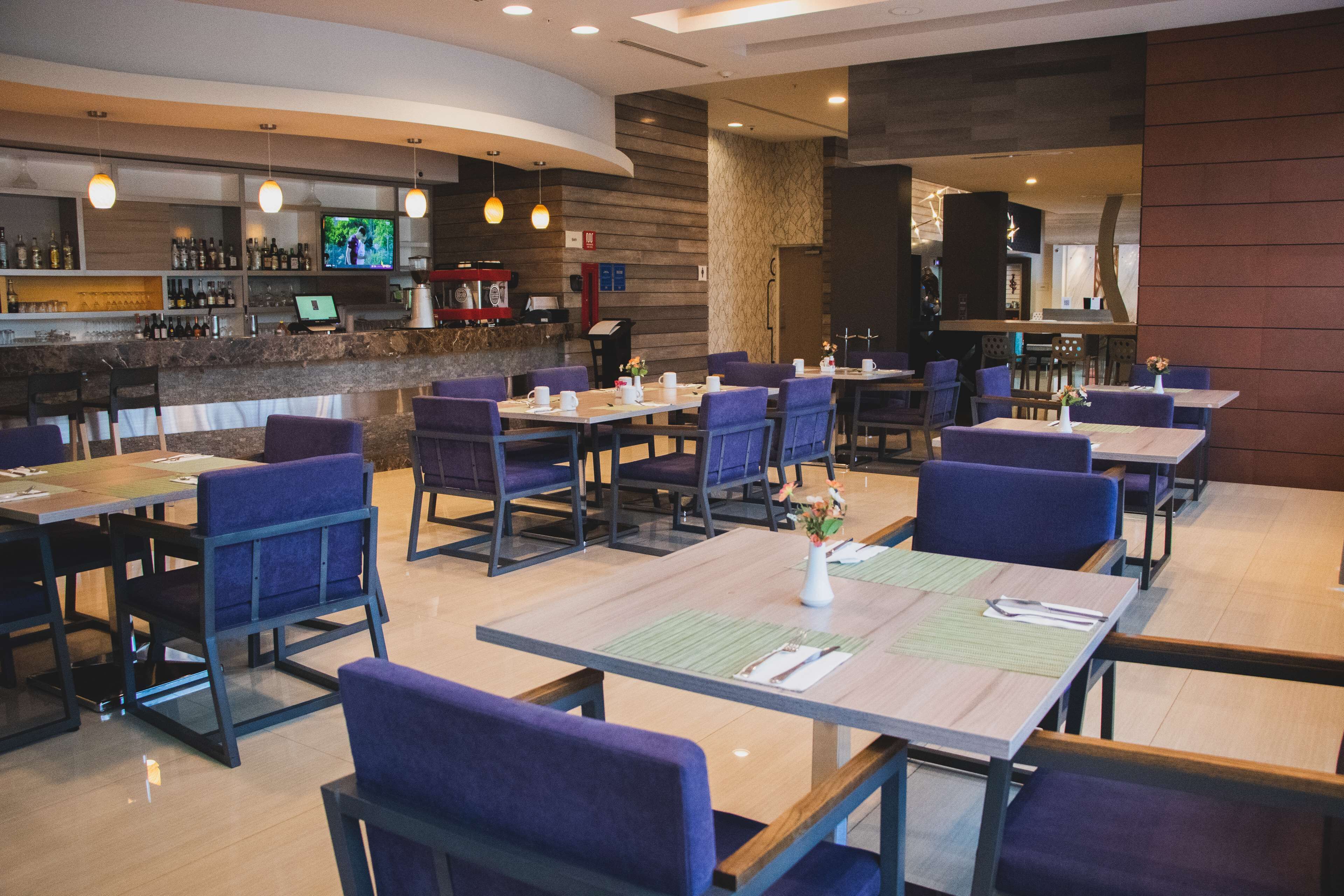 A restaurant with multiple tables and chairs, a bar area with a TV, and a counter with various items.