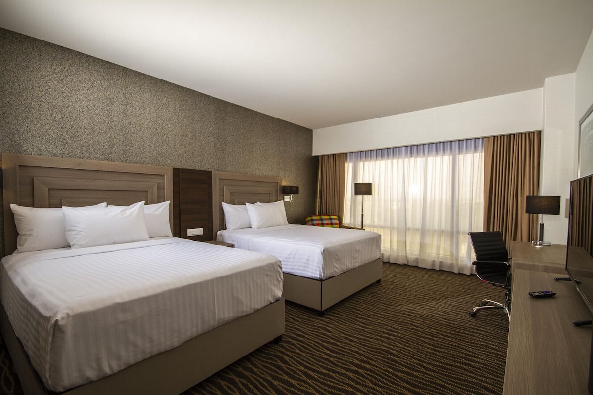 A hotel room with two beds, a desk, a chair, and a television.