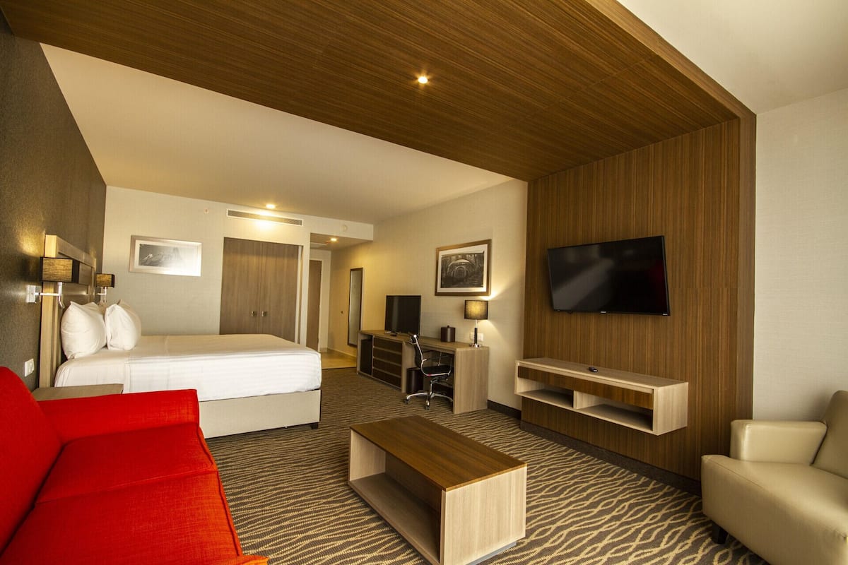 A hotel room with a bed, a TV, a desk, a chair, and a red couch.