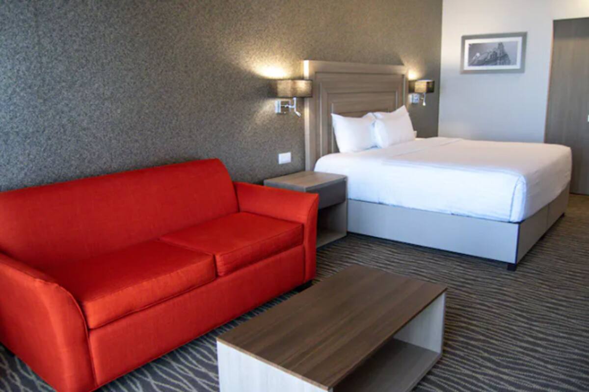 A hotel room with a red sofa, a bed, a nightstand, and a wooden side table.