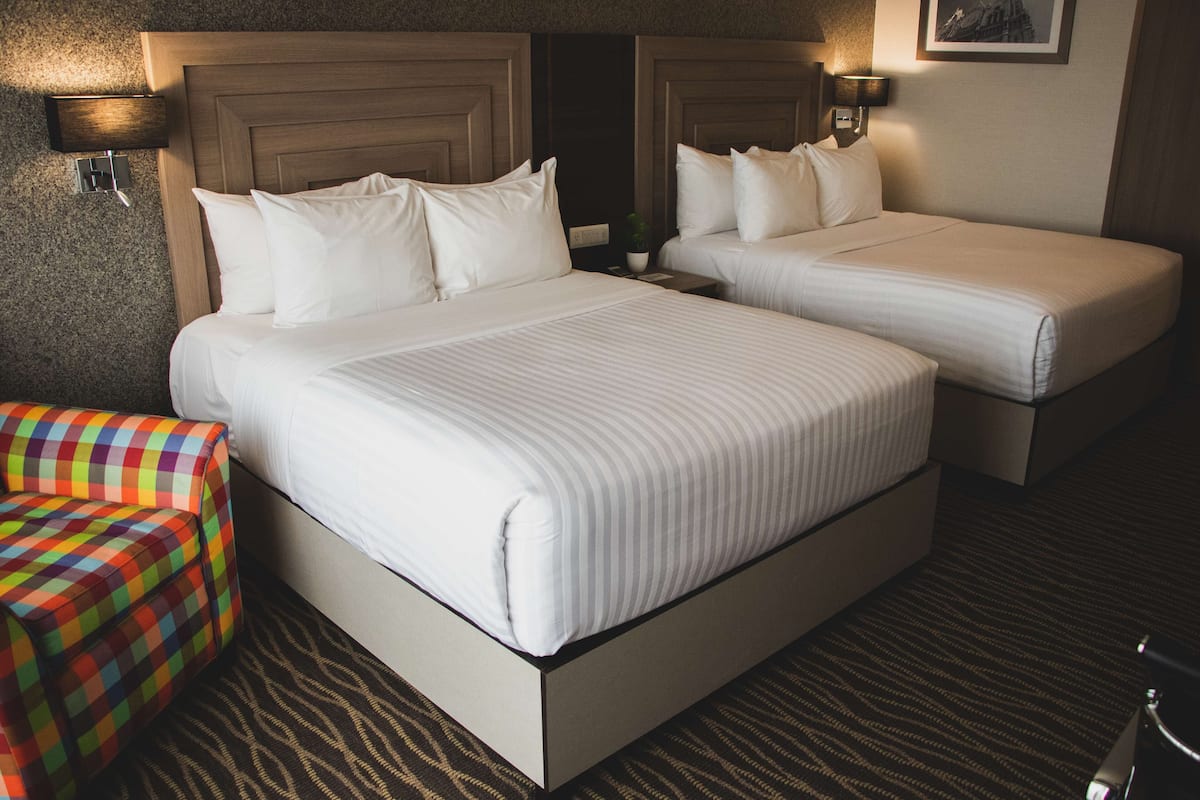 A hotel room with two beds, a colorful ottoman, and a carpeted floor.