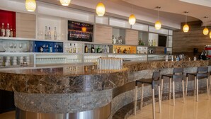 Zona de bar moderna con una barra curva de granito, varios taburetes y lámparas colgantes.