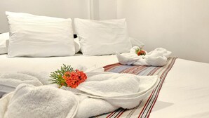 Een net opgemaakt bed met witte lakens, een bloemenarrangement en een gestreept plaid.