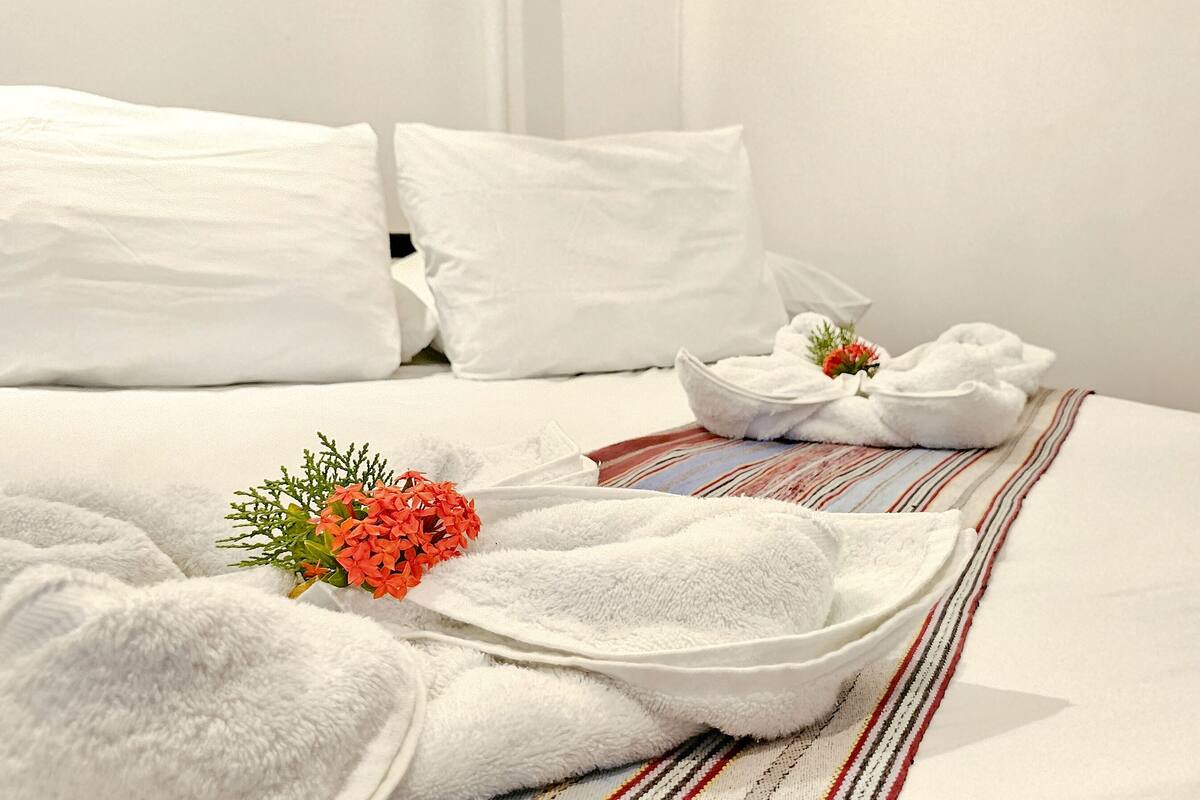 Un lit bien fait, avec du linge de lit blanc, un arrangement floral et un plaid rayé.