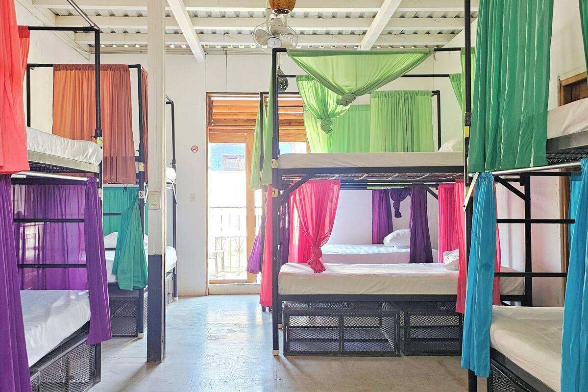 Une chambre de dortoir avec des lits superposés, chacun recouvert d’un tissu aux couleurs vives.