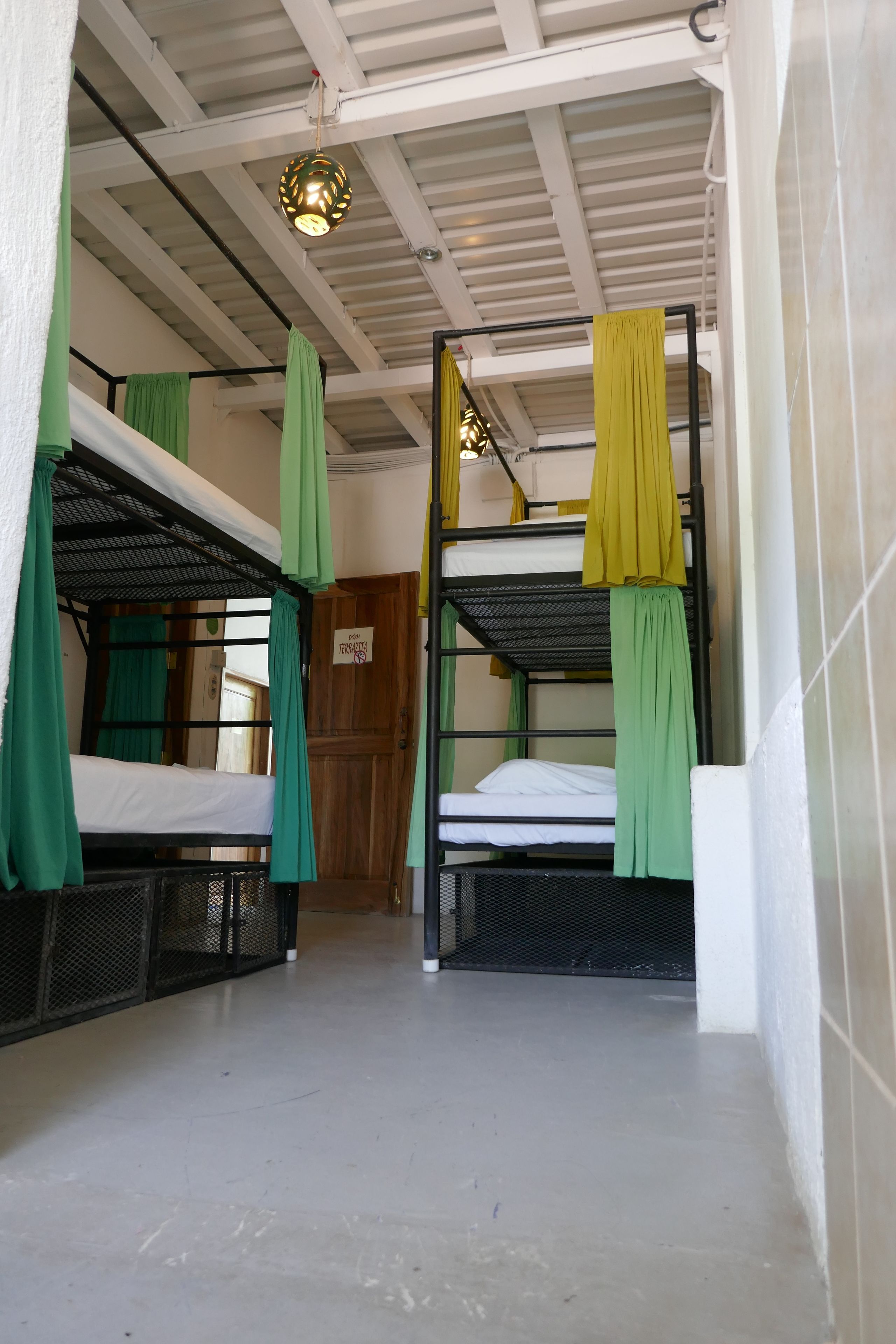A dormitory-style room with bunk beds, green and yellow curtains, and a ceiling light fixture.
