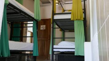 A dormitory-style room with bunk beds, green and yellow curtains, and a ceiling light fixture.