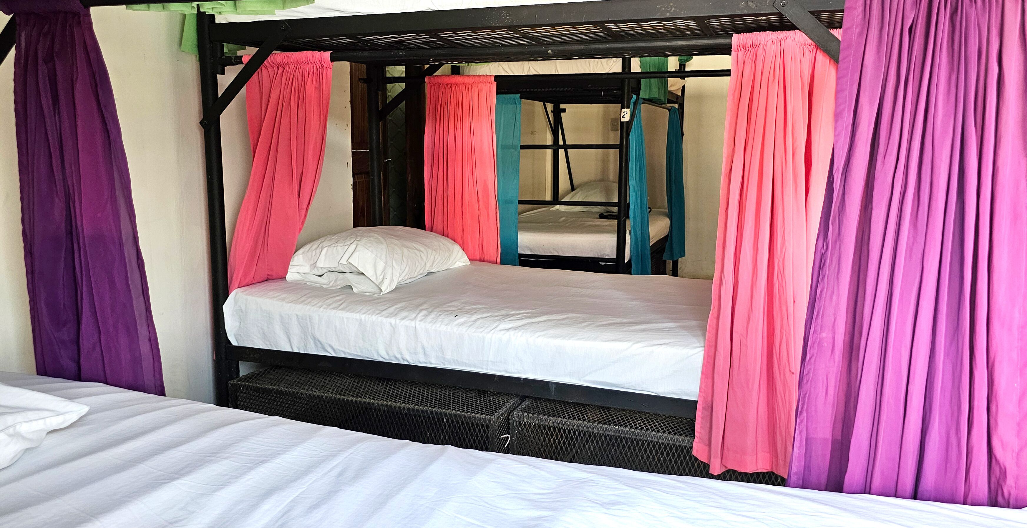 Un lit superposé avec un matelas et des oreillers, entouré de rideaux de différentes couleurs.