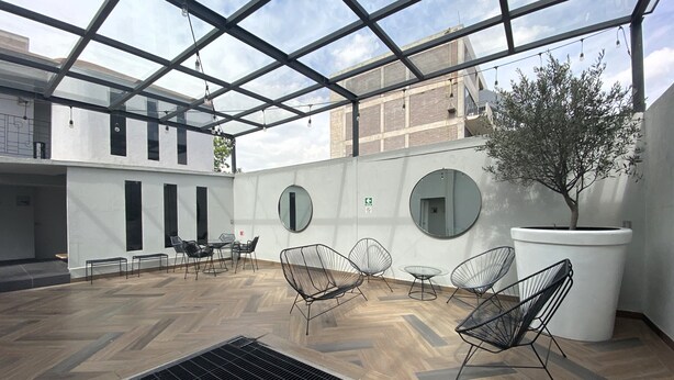 Un área de estar moderna al aire libre con techo de vidrio, piso de madera y sillas de metal.