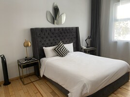 Un lit bien fait, doté d’une tête de lit capitonnée, une table de chevet avec une lampe et un miroir fixé au mur.
