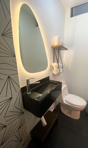 Un baño moderno con un lavamanos negro, un inodoro y un espejo grande.