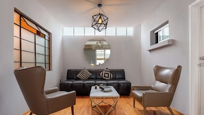 Una sala de estar moderna con un sofá de cuero, dos sillones, una mesa de centro de mármol y un espejo grande.