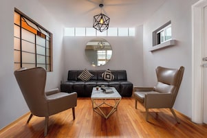 Una sala de estar moderna con un sofá de cuero, dos sillones, una mesa de centro de mármol y un espejo grande.