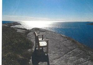 Ein Stuhl an einem felsigen Ufer mit Blick auf ein ruhiges Meer.
