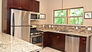 A modern kitchen with stainless steel appliances, dark wood cabinets, a granite countertop, and a window with a view of greenery. - "The Wedgewood"/A Little Bit Country, Close To Town, New, Clean And Fresh. (Kyle)